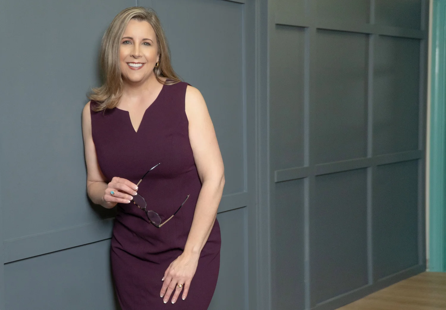 Jennifer Davis leaning against a paneled wall in a burgundy dress